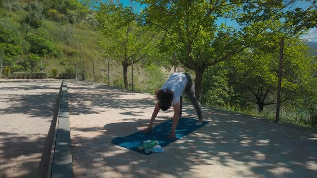 Woman practices yoga outdoors, focusing on sun salutation poses for wellness. Embracing fitness and serenity in nature, she embodies a healthy and peaceful lifestyle.