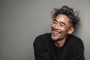 Fototapeta premium Portrait of a glad asian man in his 40s laughing while standing against blank studio backdrop