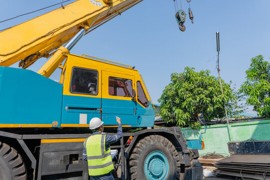 Construction worker and rigger in hard hats performing safety inspection beside mobile crane at outdoor worksite