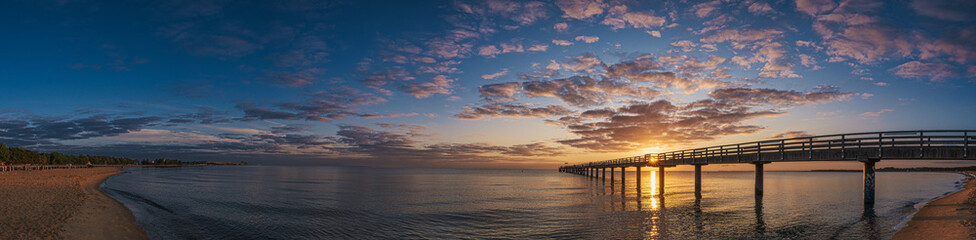 Obraz premium The pier in Boltenhagen on the Baltic Sea bathed in the warm light of sunrise.