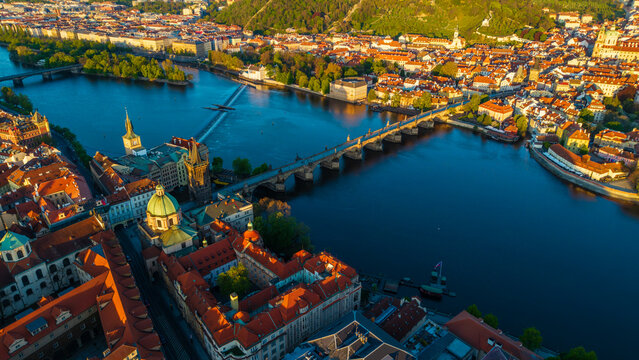 Aerial view of Charles Bridge spanning the Vltava River with historic red-tiled rooftops and the Old Town Bridge Tower under golden hour light in Prague, Prague, Czechia.