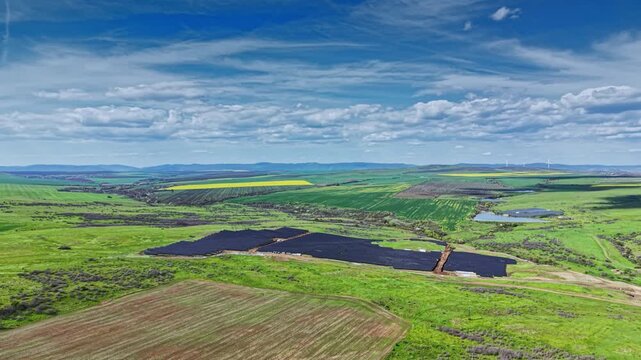 A team is finishing the installation of solar panels in a vast open field. The landscape is green with patches of crops and a clear blue sky above, indicating a focus on sustainable energy.