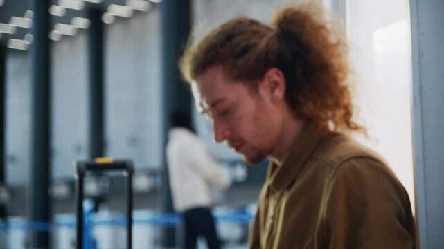 Tired man with a suitcase closing his laptop while waiting in an airport departure lounge