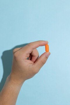 Male hand holding a pill between the fingers on a blue background. Concept of medication, treatment, drug use, and healthcare