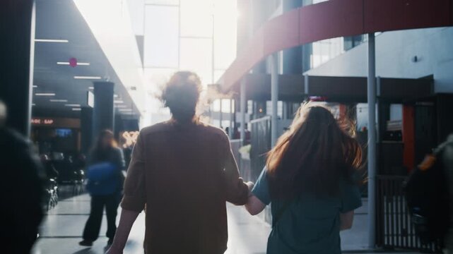 Young couple holding hands and running through a busy airport terminal to catch their flight