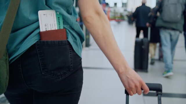 Female traveler with passport and boarding pass in pocket pulling luggage at the airport terminal