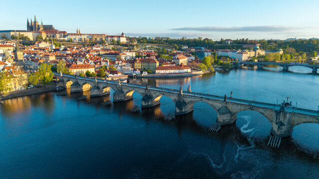 Aerial view of Charles Bridge over the Vltava River with Prague Castle and historic red rooftops in Prague, Prague, Czechia.