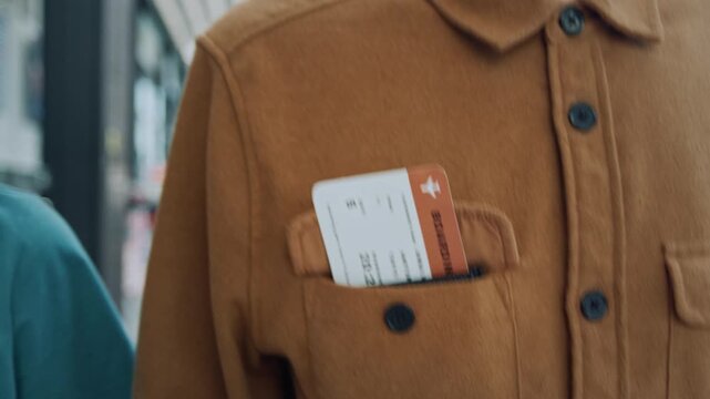A close-up shot focuses on an unrecognizable person's jacket pocket, where a folded boarding pass is clearly visible.
