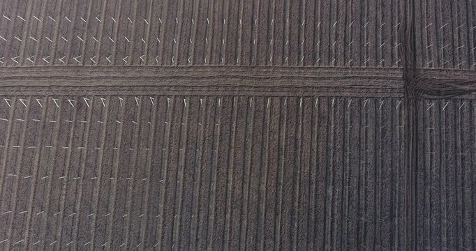 Aerial top-down view of a plowed farmland field with parallel furrows and white planting stakes during early spring soil preparation under soft overcast light