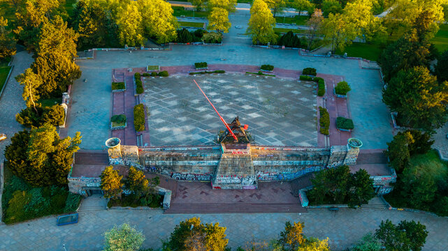 Aerial view of the Prague Metronome in Letna Park with its red needle, graffiti-covered stone base, and surrounding lush green trees under warm sunlight Prague, Prague, Czechia.