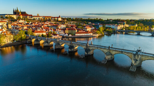 Aerial view of Charles Bridge and Prague Castle with historic red rooftops and the Vltava River during golden hour in Prague, Prague, Czechia.