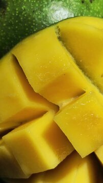 Vertical 4K macro of sliced ripe mango. Close-up of juicy yellow fruit pulp with sunlight reflections and water drops.