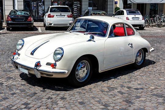 Switzerland, Zurich - June 16, 2012: Classic Porsche 356 with red interior parked in a busy plaza among modern cars and cyclists on a sunny day