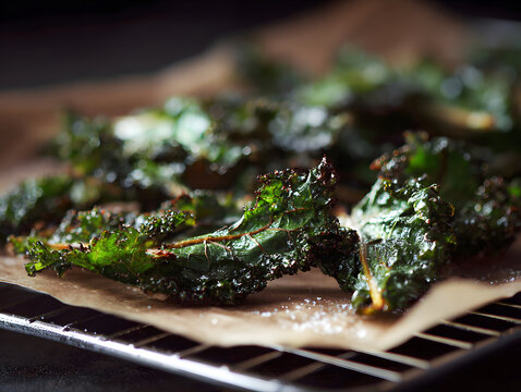 Crispy kale chips with emerald edges and sea salt flakes on parchment, close up of textured roasted green leaves with olive oil sheen and rustic serving surface