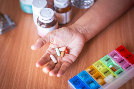 Senior woman's hand holding a variety of medical pills, preparing to take her daily dose from a pillbox. Concept of geriatric healthcare, managing multiple medications, and pharmaceutical treatment.