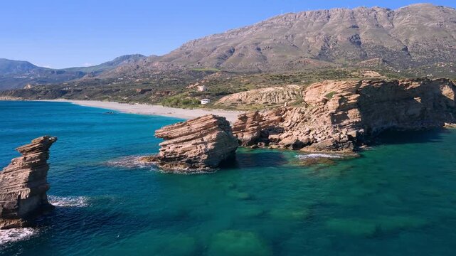 Aerial close-up flight over Triopetra beach three rocks stacks in South Crete, Greece. Drone view of wild empty beach, turquoise sea and giant geological formations at sunny day. Scenic coast, 4k.