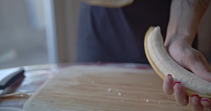 Close-up of a woman's hands skillfully peeling and then slicing a ripe banana on a wooden cutting board. Perfect for showcasing healthy eating, food preparation, and fresh fruit.