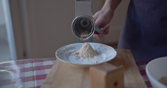 Hands operate a classic manual grinder, creating fresh breadcrumbs for cooking. This captures the essence of homemade food preparation with traditional kitchen tools.