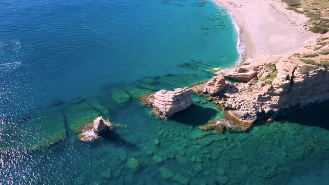Aerial pull back flight over Triopetra beach three rocks stacks in South Crete, Greece. Drone reveal of wild empty beach, vertical cliffs and mountains at sunny day. Scenic coast landscape, 4k.