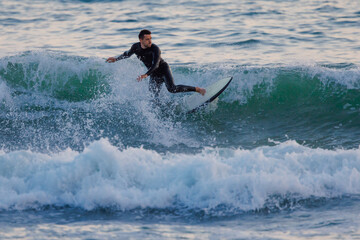 Obraz premium Surfer on surfboard riding ocean wave at evening light