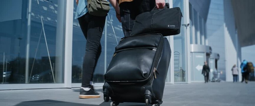 Unrecognizable couple holding hands and walking with a suitcase outside a modern airport terminal