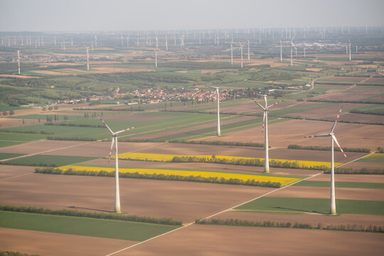 Aerial view of wind turbines standing in a patchwork of green and yellow agricultural fields near a small village in Lower Austria, Austria.