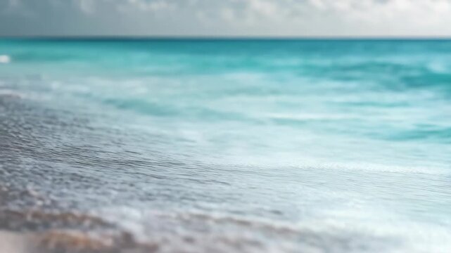 A tranquil beach scene featuring a calm ocean with light waves gently lapping onto the shore under a clear sky.