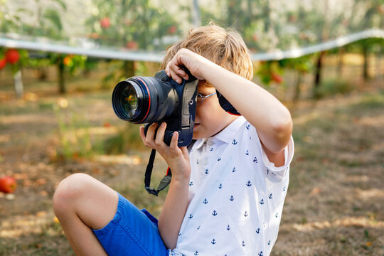 Young boy taking photos with a DSLR camera in an apple orchard, sitting outdoors during harvest season, creative hobby and real life childhood moment.