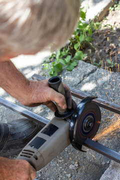 Elderly man using angle grinder to cut metal bars outdoors