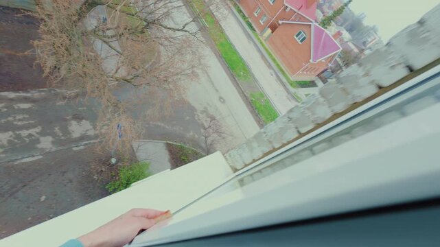 A man washes the glass of a plastic window outside the apartment with a sponge. The cleaner provides cleaning services for dirty windows at height. From the first person.