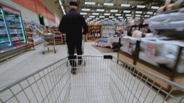 Timelapse from a shopping cart in family hypermarket, fast moving through supermarket aisle. Food store, grocery shop. POV customer trolley moving into mall. Shelves of products. Immersive experience