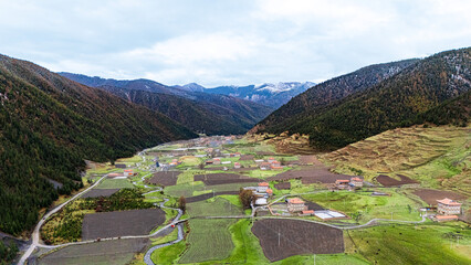 Aerial view of Jiagenba village in Sichuan, terraced farmlands nestled in mountain valley with autumn hues and Tibetan plateau scenery © jiahong