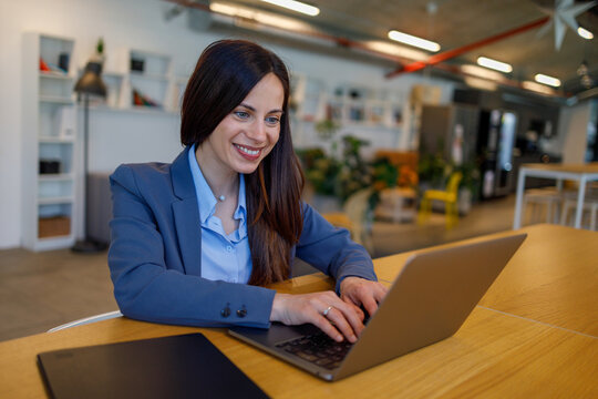 Businesswoman smiling operating laptop in modern office