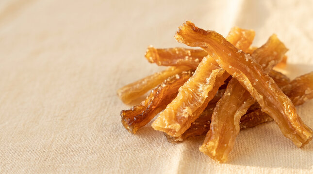 Dried melon strips pile macro on cream linen background, traditional kak snack with amber caramelized texture and natural sugars visible .