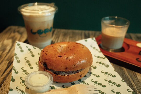 4 MAY 2026, Bangkok Thailand: Close-up of a bagel with cream cheese and beverages on a wooden table at Loro Specialty Coffee cafe.