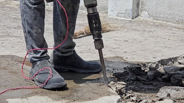 An electric jackhammer is used to break up a concrete rooftop or patio surface. This specialized construction work is essential for preparing the structure for professional home repair waterproofing.