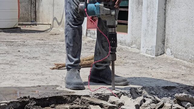 A worker uses an electric jackhammer to break up a concrete surface. This specific work on an outdoor rooftop or patio area, being steadily performed as a part of residential home repair waterproofing