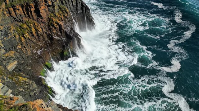 Powerful ocean waves crashing against a rugged rocky cliff, dramatic coastal landscape with sea spray and foam, highangle view of the atlantic coastline