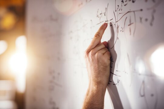 Man's hand pointing at complex math equation on whiteboard