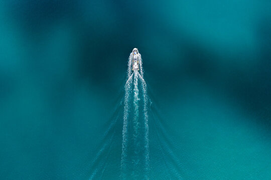 Aerial view of a small white boat leaving a white wake in the turquoise sea near the Itoshima Peninsula Itoshima, Fukuoka, Japan.