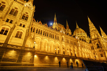 Fototapeta premium Stunning Night View of the Hungarian Parliament Building in Budapest, illuminated Gothic Revival Architecture with Golden Lights against a Dark Sky at Nighttime.