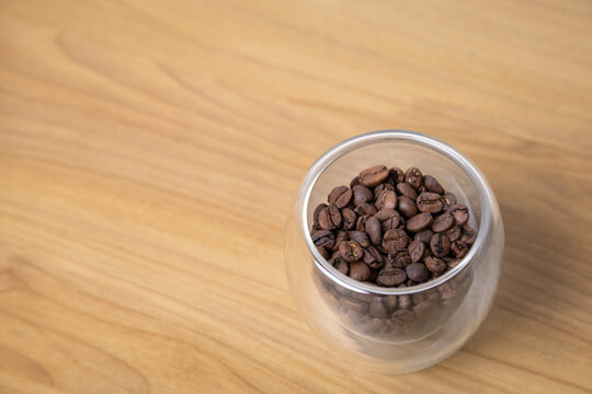 Gr&atilde;os de caf&eacute; torrados em copo para caf&eacute; em mesa de madeira