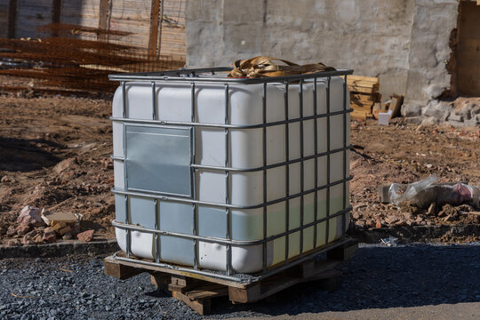 White Industrial IBC Tote Water Tank in Metal Cage on Construction Site Pallet