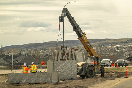 Calgary, Alberta, Canada. May 5, 2026. Construction workers use a SANY telehandler to install stone sound wall panels along a suburban road.