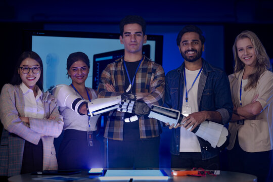 diverse robotics engineering team poses in an RD lab. The engineers, including an Indian woman, proudly display their new AI-powered prosthetic arm prototype.
