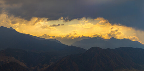 Obraz premium Dramatic Mountain Range Silhouette at Sunset with Golden Clouds