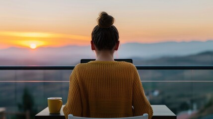 Fototapeta premium A tranquil scene of a woman working remotely on her laptop from a balcony during a vibrant sunset with a scenic mountain view and a warm drink embodying a peaceful lifestyle