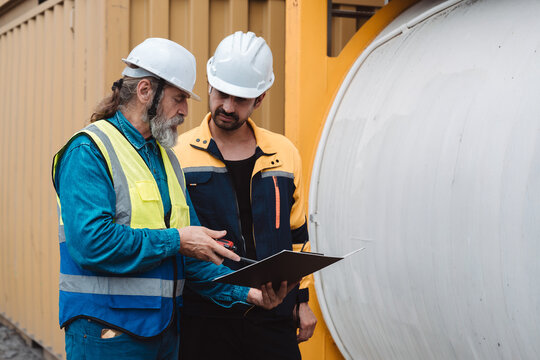 Industrial engineers discussing logistics and tank container maintenance. Senior caucasian worker and colleague talking about chemical storage at yard.