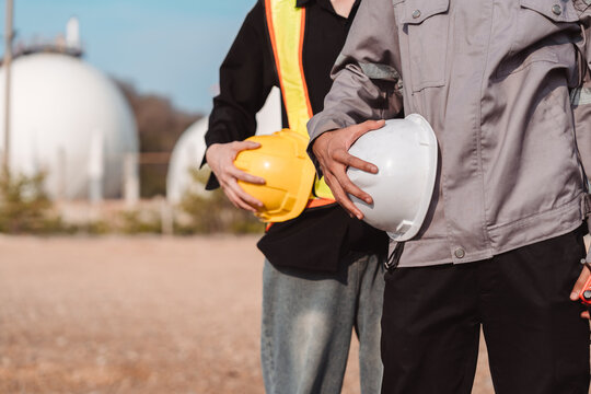 Industrial safety protection and energy infrastructure management. Male and female workers carrying helmets for project coordination at gas storage tank site.