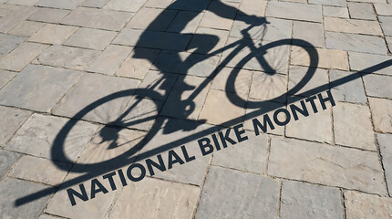 Naklejka premium A sharp shadow of a person riding a bicycle cast upon a textured stone pavement during a bright sunny day with text reading national bike month displayed clearly on the ground surface